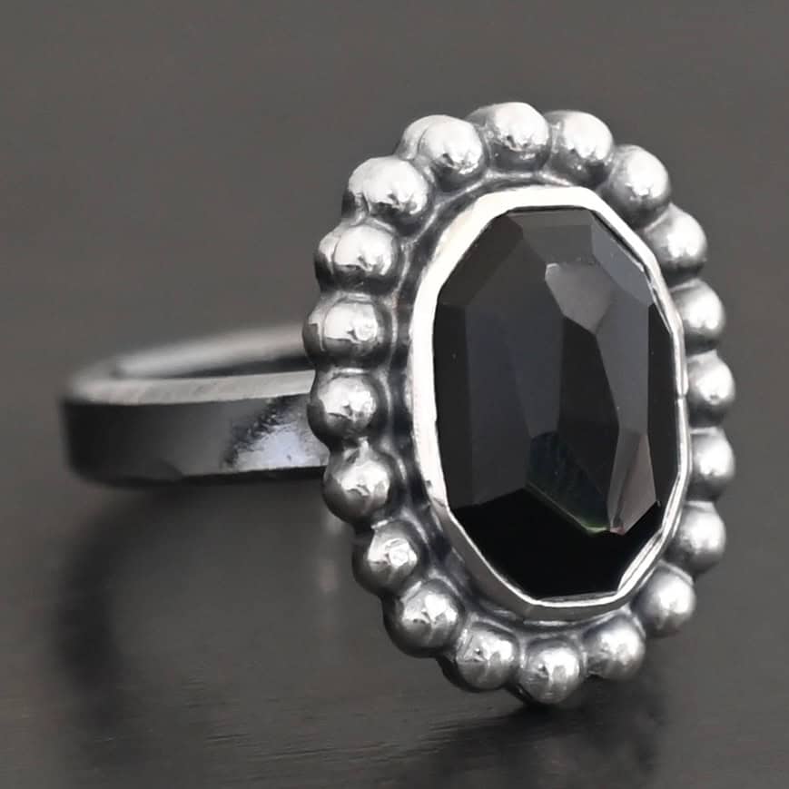 "Midnight Skies" Ring. Sterling Silver & Black Onyx. There is an oval, vertical black onyx in the center with balls of silver circling all the way around it. Ring band is smooth & lightly oxidized.