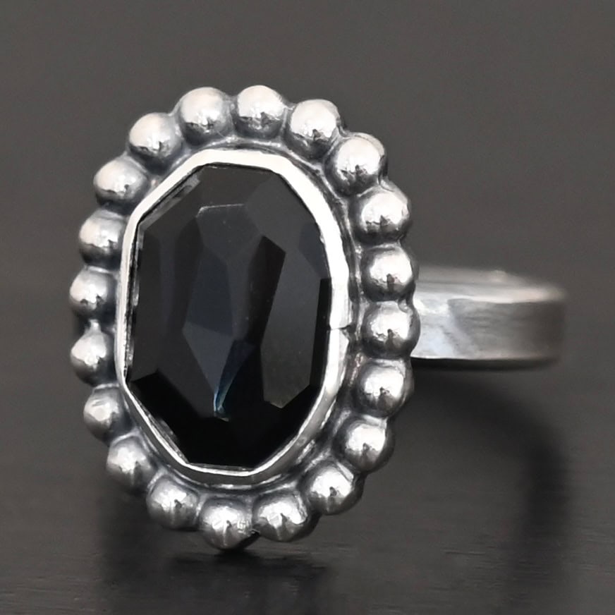 "Midnight Skies" Ring. Sterling Silver & Black Onyx. There is an oval, vertical black onyx in the center with balls of silver circling all the way around it. Ring band is smooth & lightly oxidized.