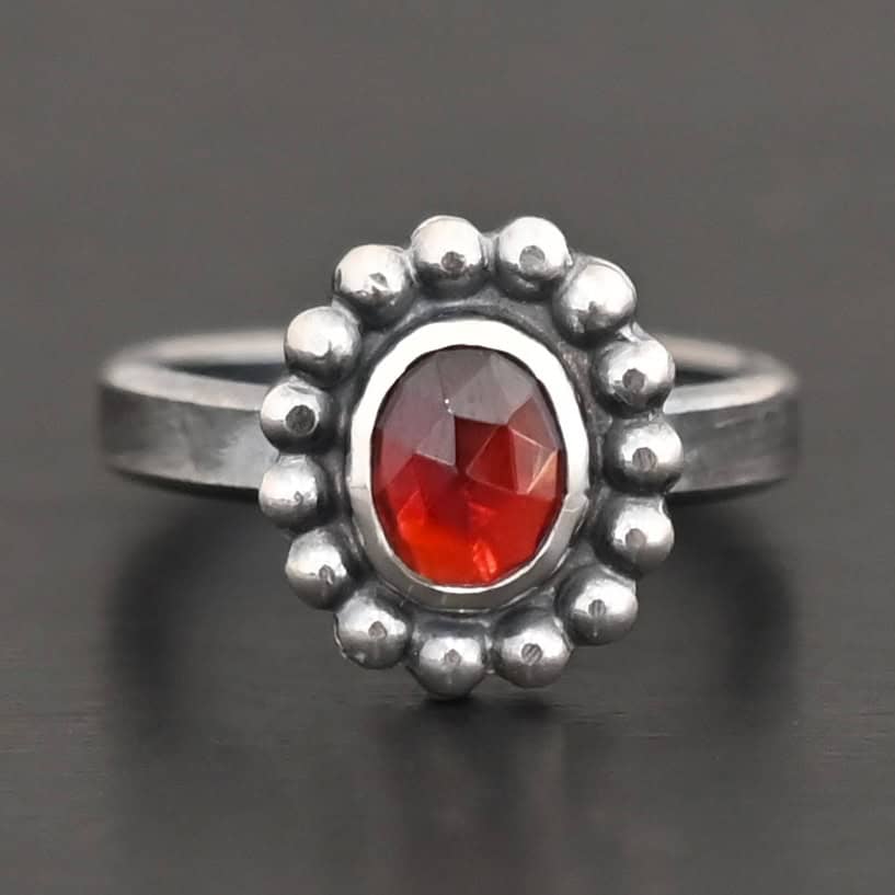 Rowan Ring "Rowan" Ring. Sterling Silver & Garnet. There is an oval, vertical garnet in the center with balls of silver circling all the way around it. Ring band is smooth & lightly oxidized.