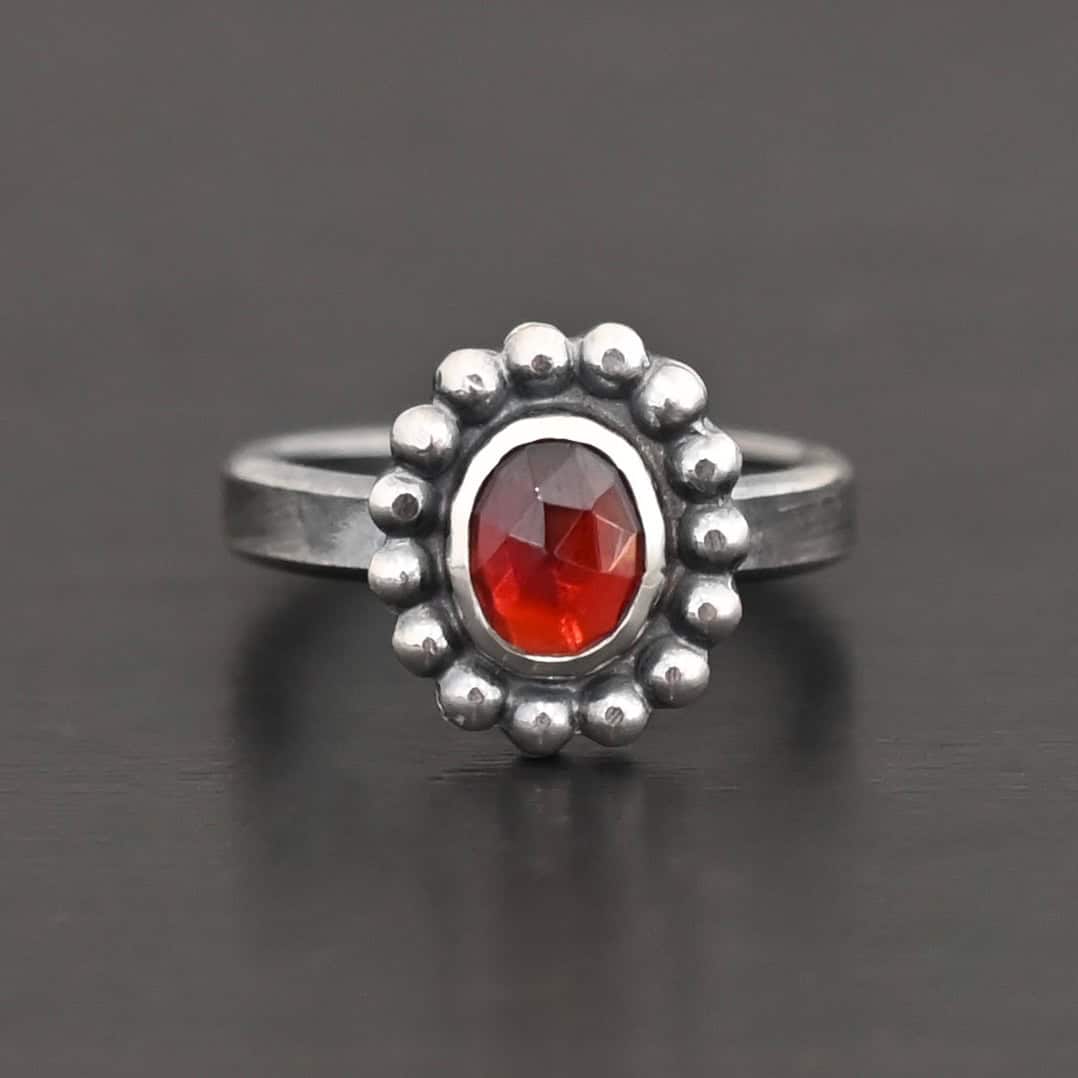 Rowan Ring "Rowan" Ring. Sterling Silver & Garnet. There is an oval, vertical garnet in the center with balls of silver circling all the way around it. Ring band is smooth & lightly oxidized.
