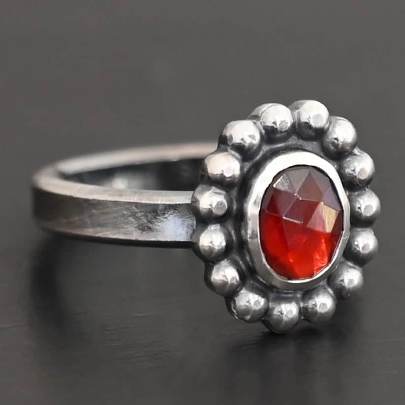 Rowan Ring "Rowan" Ring. Sterling Silver & Garnet. There is an oval, vertical garnet in the center with balls of silver circling all the way around it. Ring band is smooth & lightly oxidized.