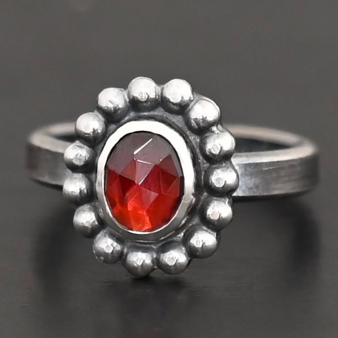 Rowan Ring "Rowan" Ring. Sterling Silver & Garnet. There is an oval, vertical garnet in the center with balls of silver circling all the way around it. Ring band is smooth & lightly oxidized.