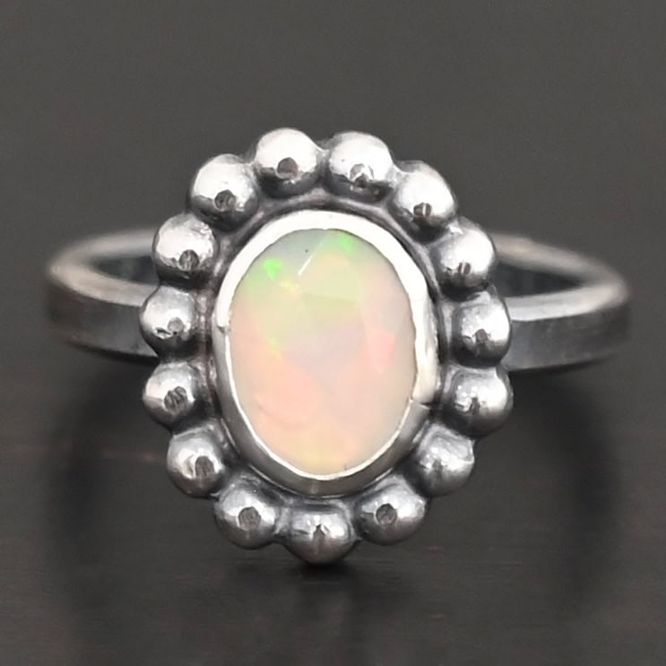 "Honeysuckle" Ring. Sterling Silver & Opal. There is an oval, vertical opal in the center with balls of silver circling all the way around it. Ring band is smooth & lightly oxidized.