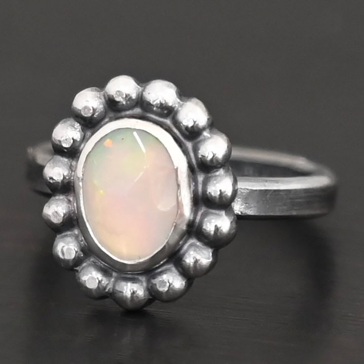 "Honeysuckle" Ring. Sterling Silver & Opal. There is an oval, vertical opal in the center with balls of silver circling all the way around it. Ring band is smooth & lightly oxidized.