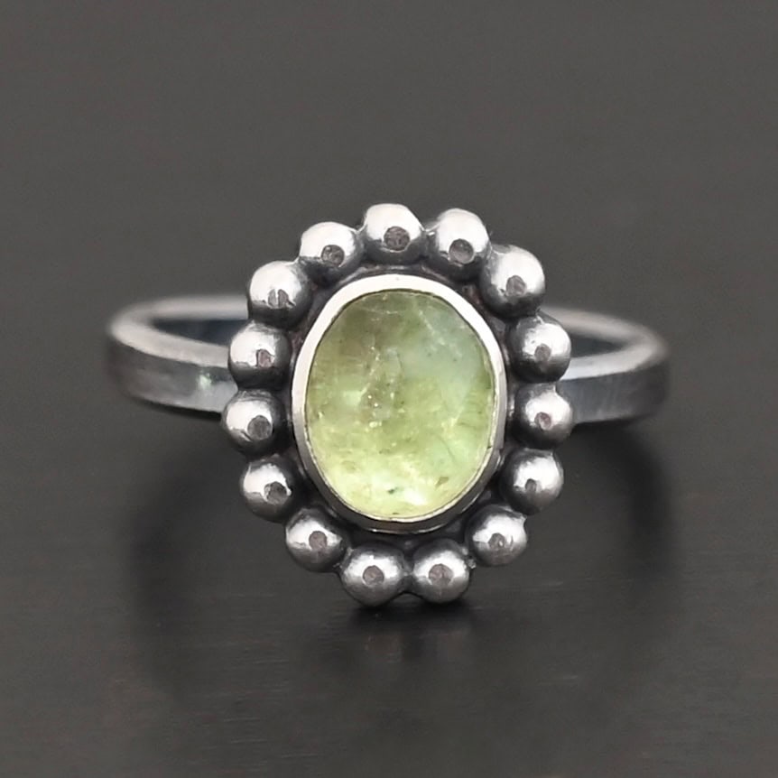 Maven Ring "Maven" Ring. Sterling Silver & Tourmaline. There is an oval, vertical tourmaline in the center with balls of silver circling all the way around it. Ring band is smooth & lightly oxidized.