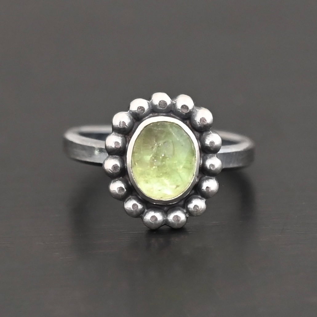 Maven Ring "Maven" Ring. Sterling Silver & Tourmaline. There is an oval, vertical tourmaline in the center with balls of silver circling all the way around it. Ring band is smooth & lightly oxidized.