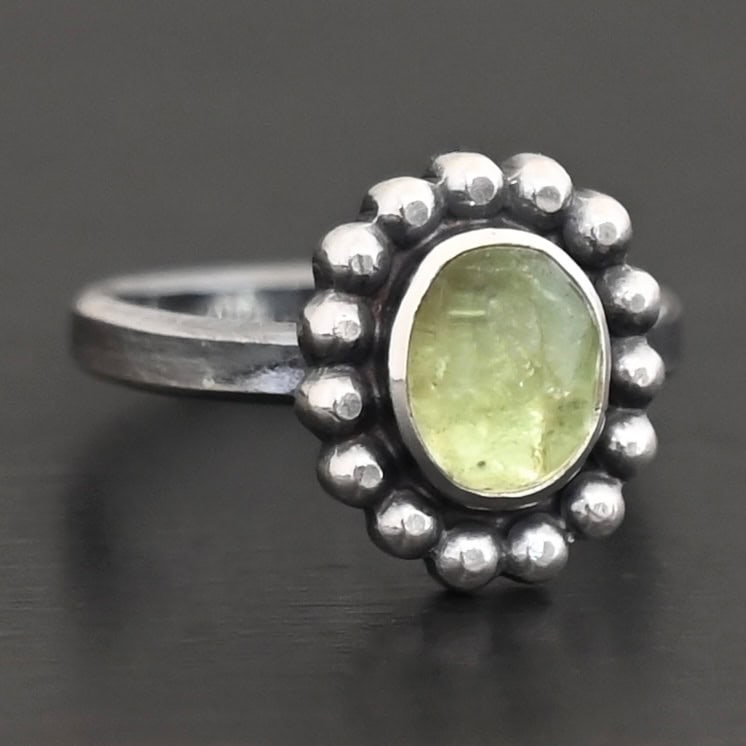 Maven Ring "Maven" Ring. Sterling Silver & Tourmaline. There is an oval, vertical tourmaline in the center with balls of silver circling all the way around it. Ring band is smooth & lightly oxidized.