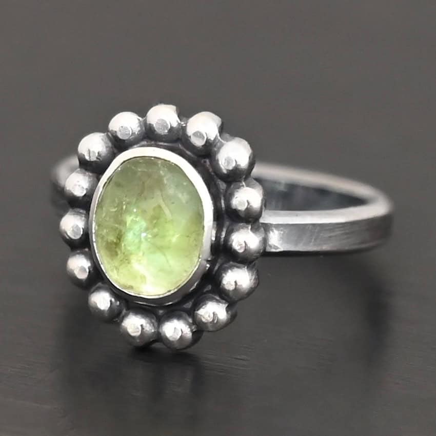 Maven Ring "Maven" Ring. Sterling Silver & Tourmaline. There is an oval, vertical tourmaline in the center with balls of silver circling all the way around it. Ring band is smooth & lightly oxidized.