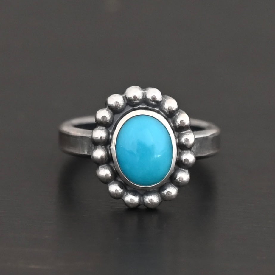 "Sky & Spirit" Ring. Sterling Silver & Turquoise. There is an oval, vertical turquoise in the center with balls of silver circling all the way around it. Ring band is smooth & lightly oxidized.