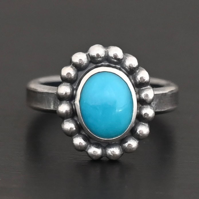 "Sky & Spirit" Ring. Sterling Silver & Turquoise. There is an oval, vertical turquoise in the center with balls of silver circling all the way around it. Ring band is smooth & lightly oxidized.