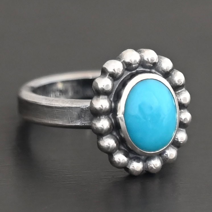 "Sky & Spirit" Ring. Sterling Silver & Turquoise. There is an oval, vertical turquoise in the center with balls of silver circling all the way around it. Ring band is smooth & lightly oxidized.