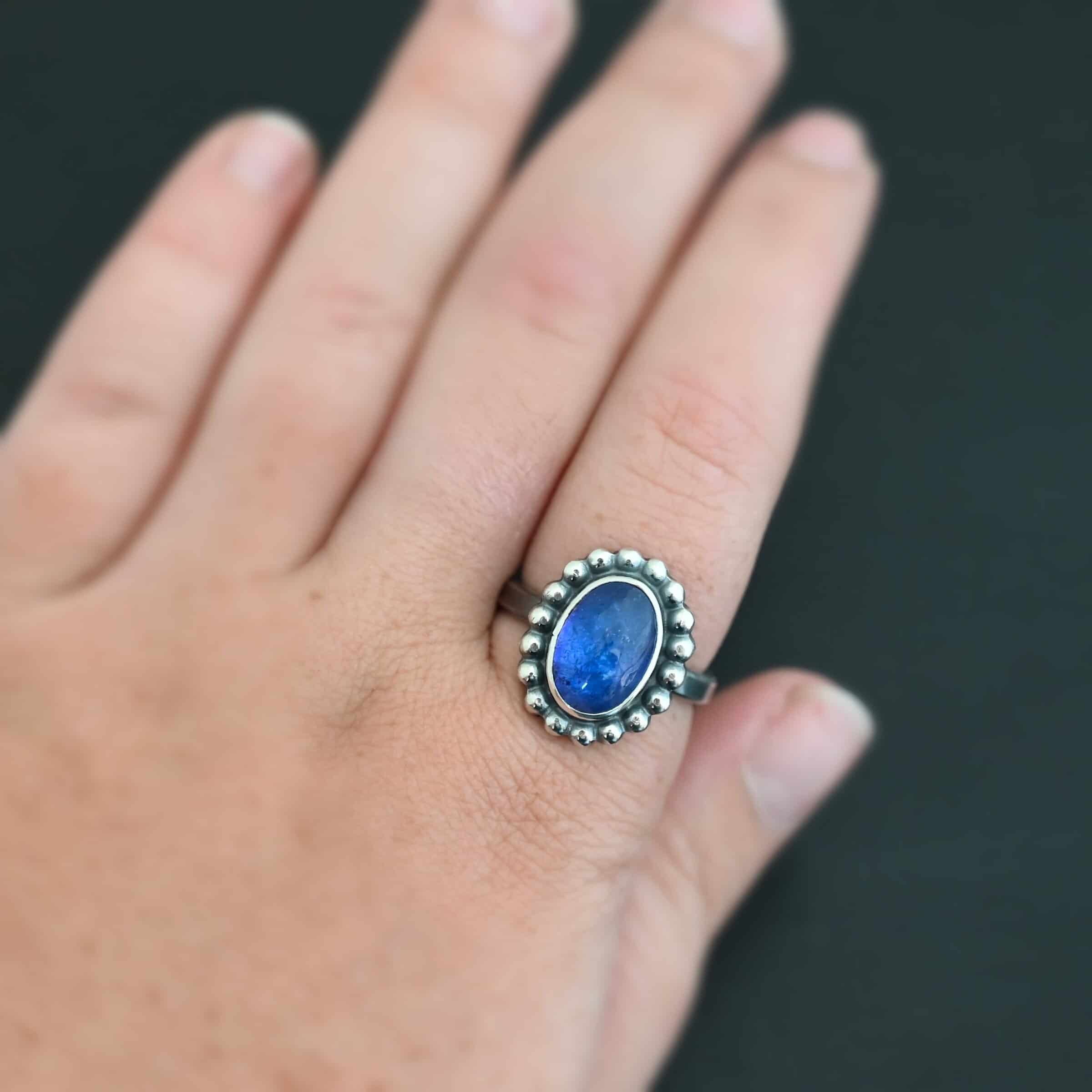 "Asena" Ring. Sterling Silver & Tanzanite. There is an oval, vertical tanzanite in the center with balls of silver circling all the way around it. Ring band is smooth & lightly oxidized.