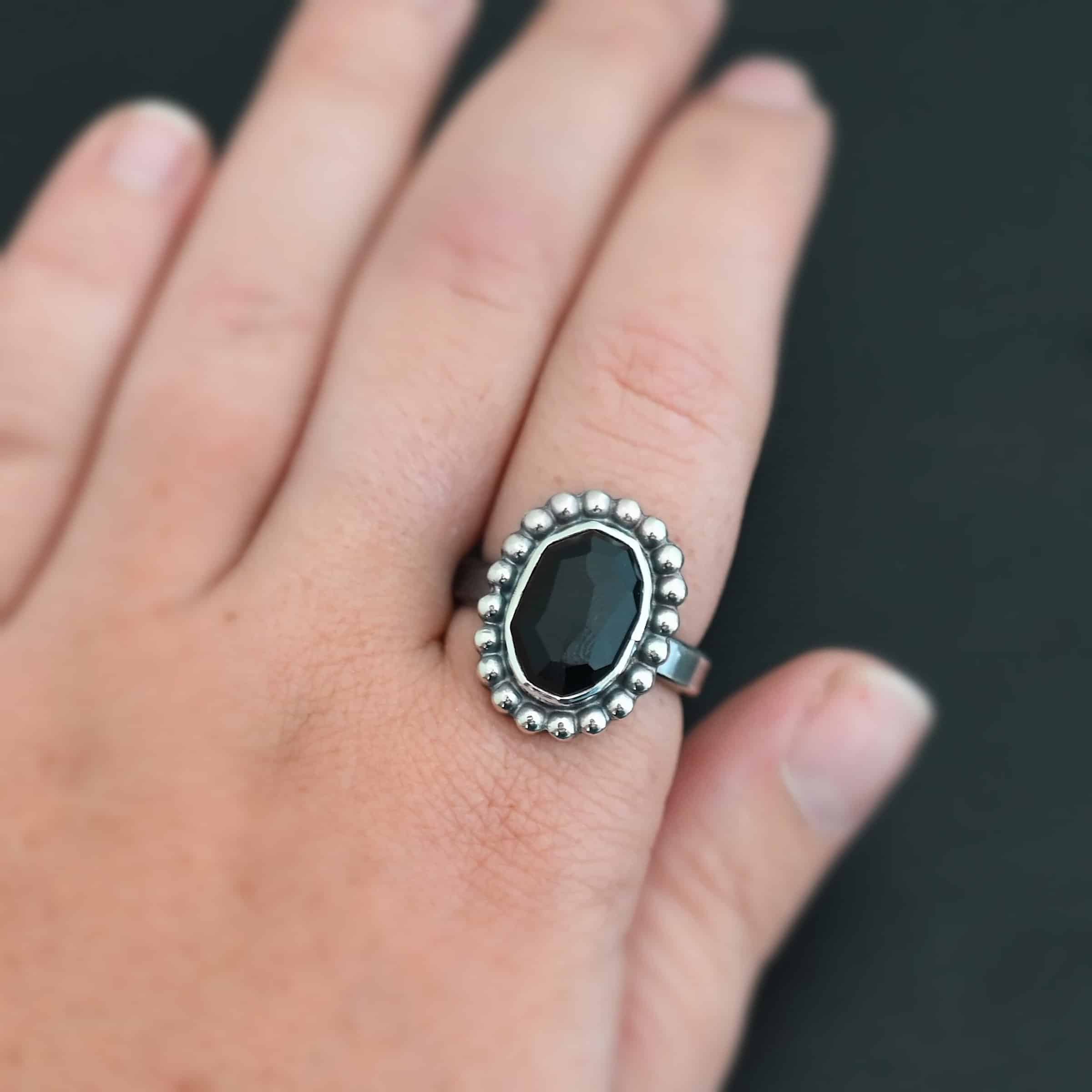 "Midnight Skies" Ring. Sterling Silver & Black Onyx. There is an oval, vertical black onyx in the center with balls of silver circling all the way around it. Ring band is smooth & lightly oxidized.