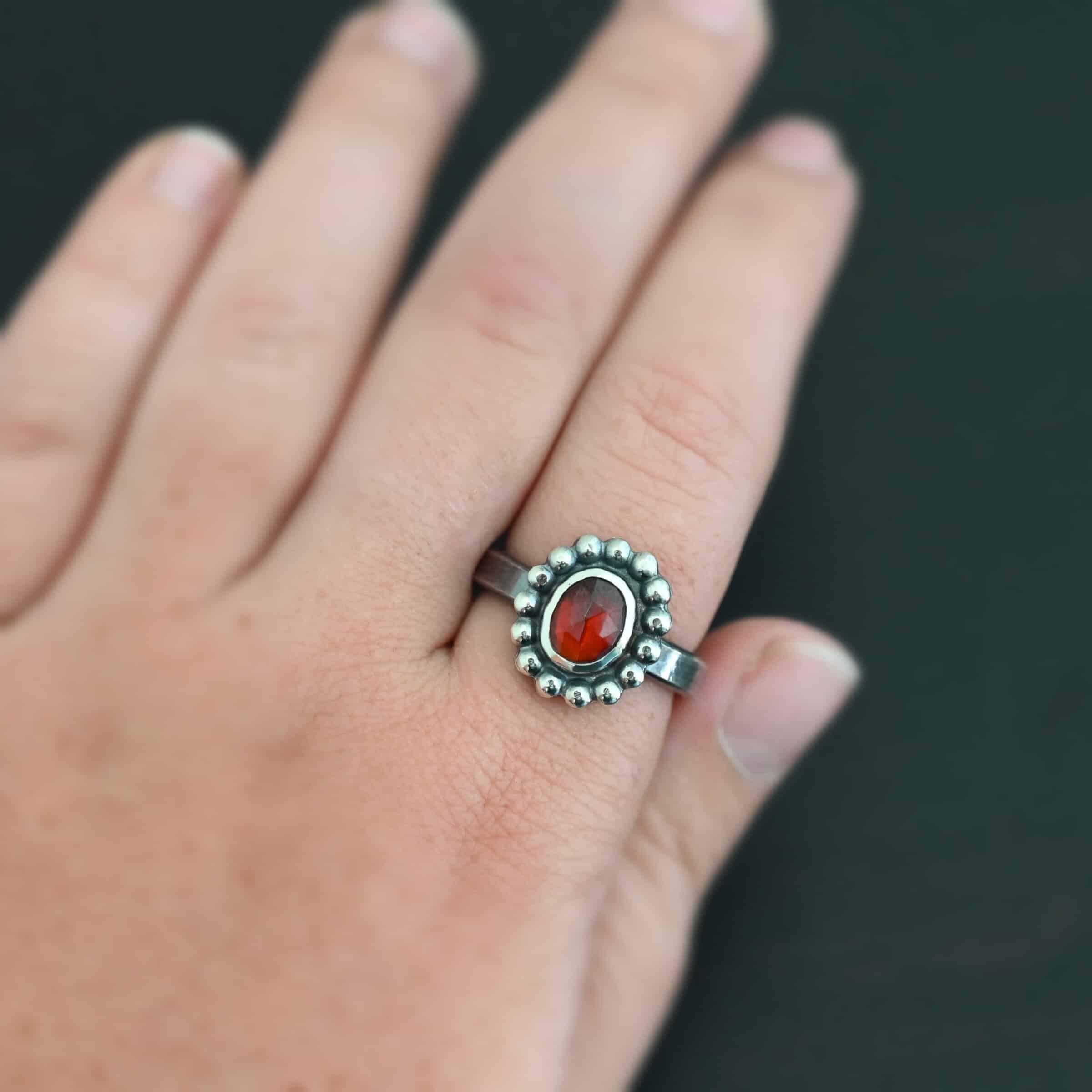 Rowan Ring "Rowan" Ring. Sterling Silver & Garnet. There is an oval, vertical garnet in the center with balls of silver circling all the way around it. Ring band is smooth & lightly oxidized.