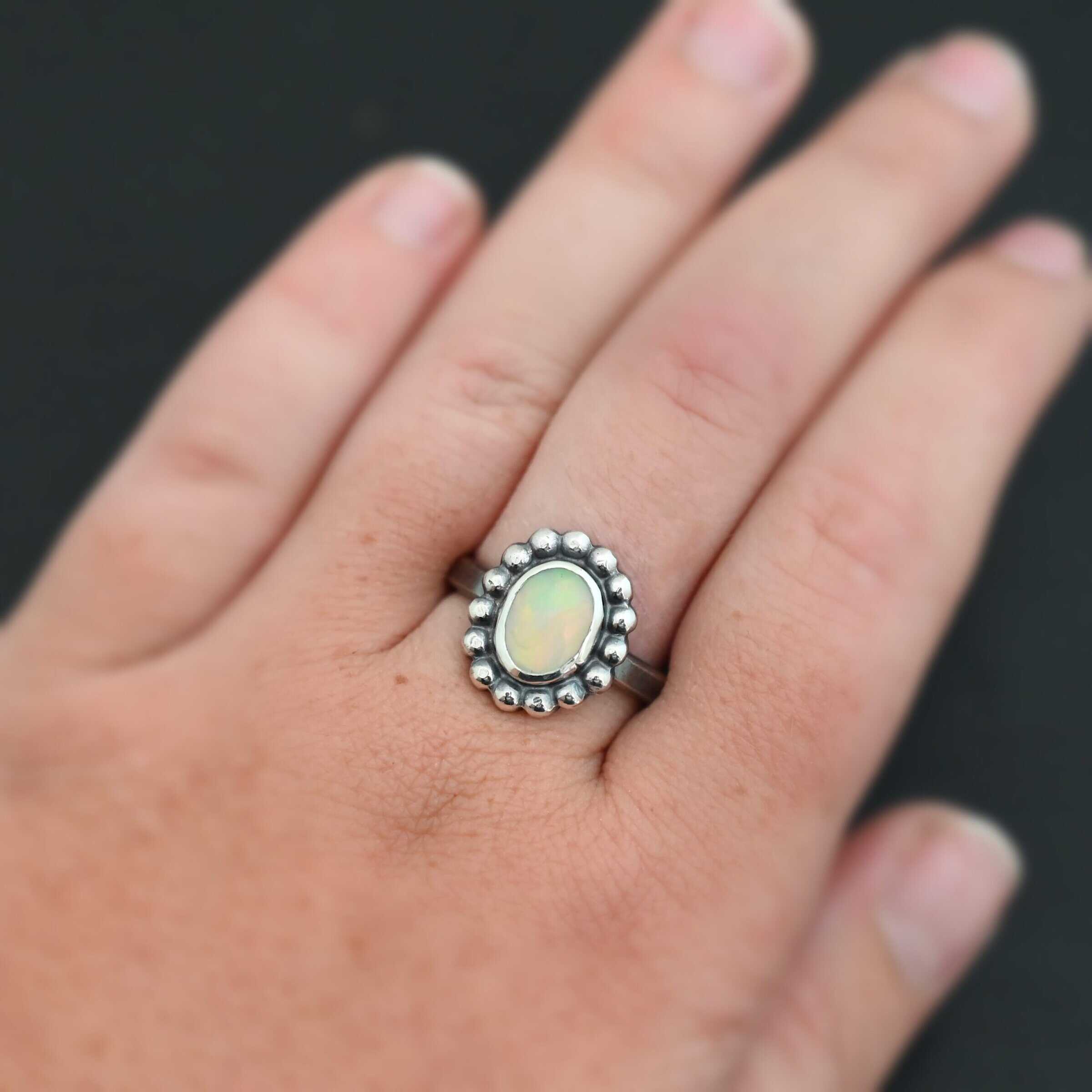 "Honeysuckle" Ring. Sterling Silver & Opal. There is an oval, vertical opal in the center with balls of silver circling all the way around it. Ring band is smooth & lightly oxidized.