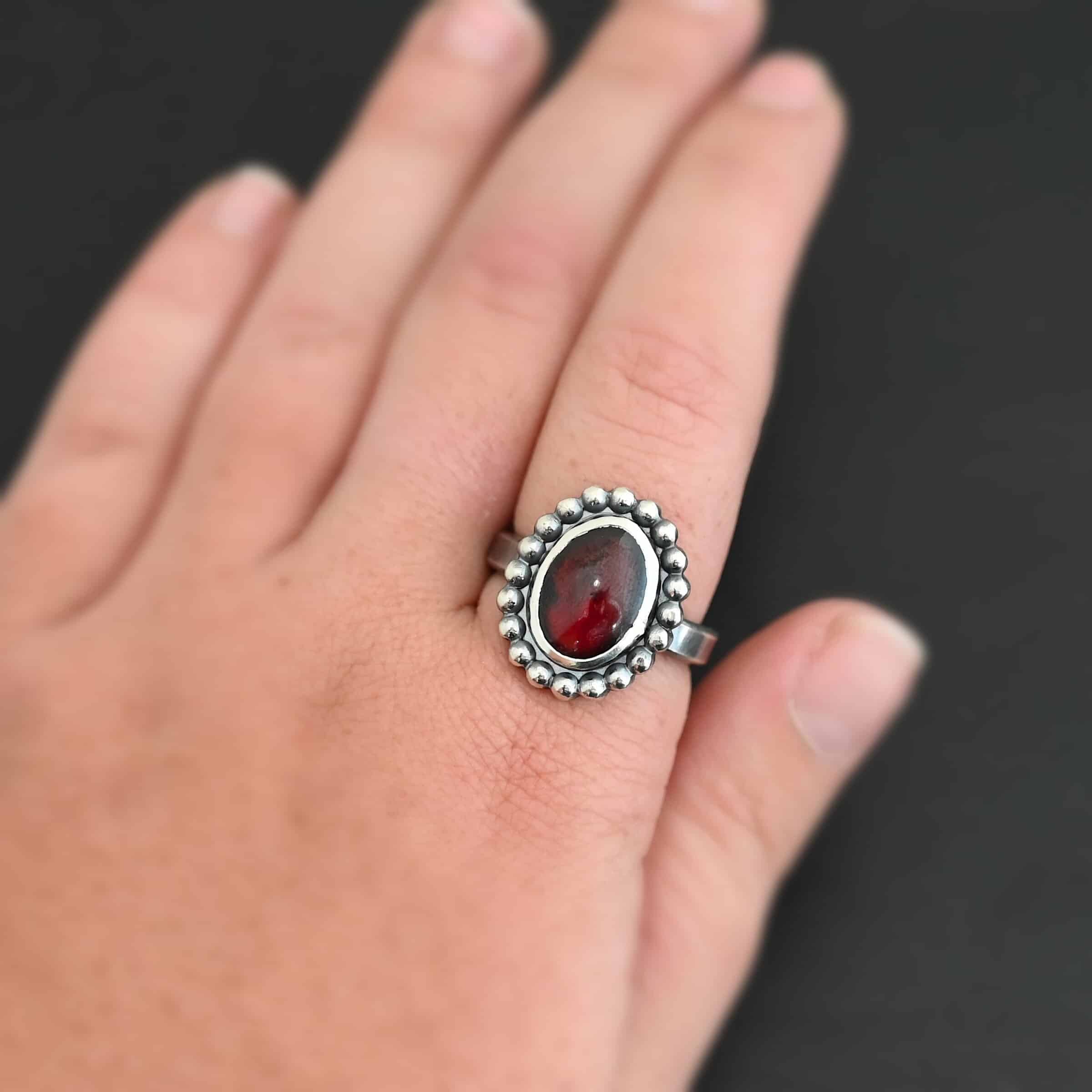Deep Satin Ring "Deep Satin" Ring. Sterling Silver & Garnet. There is an oval, vertical garnet in the center with balls of silver circling all the way around it. Ring band is smooth & lightly oxidized.