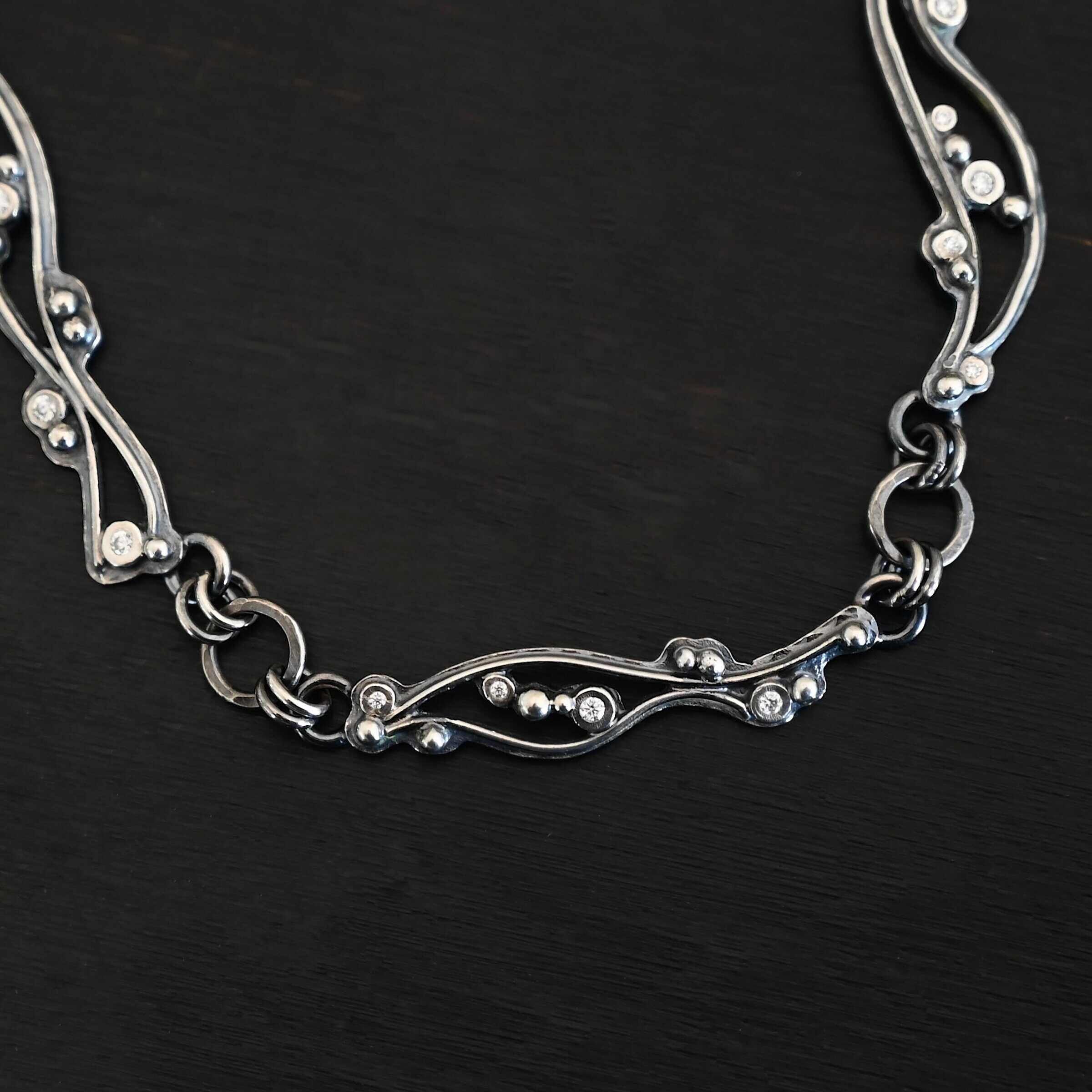 Dorthea Necklace "Dorthea" Necklace. There are nine wavy pieces of silver connected together in a collar necklace. Each piece has silver ball detail and multiple moissanites surrounding them. The lines on the waves are hammered lightly.