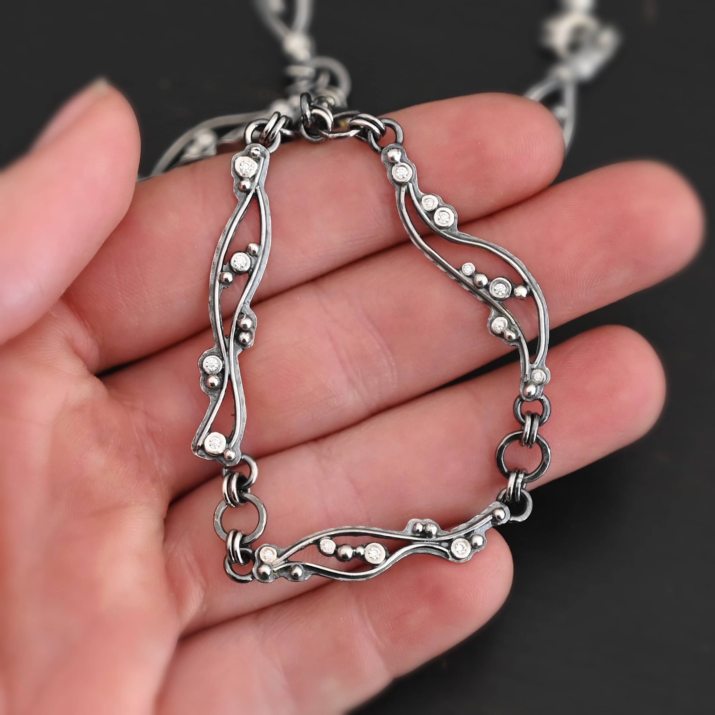 Dorthea Necklace "Dorthea" Necklace. There are nine wavy pieces of silver connected together in a collar necklace. Each piece has silver ball detail and multiple moissanites surrounding them. The lines on the waves are hammered lightly.