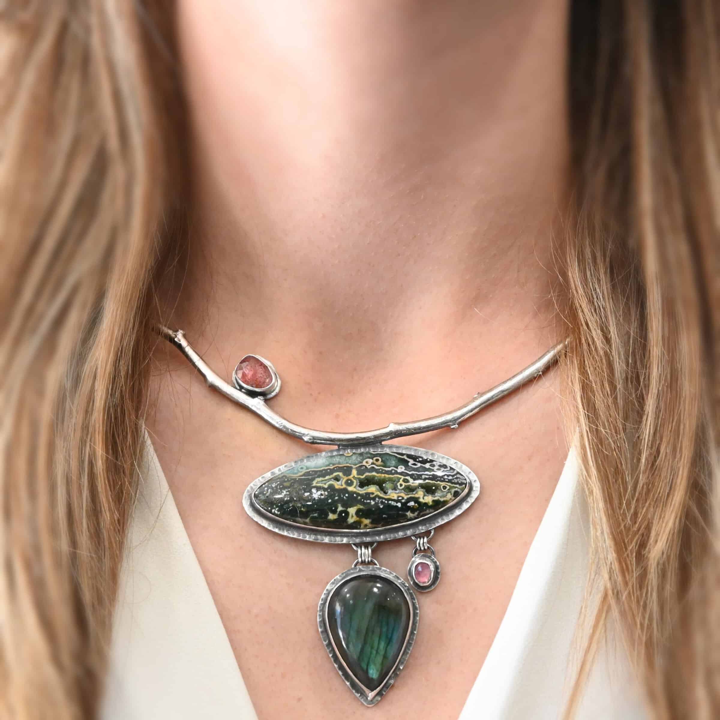 In The Darkness, There Is Light Necklace "In The Darkness, There is Light" Necklace. There is a large, curved, sterling silver casted twig. Soldered beneath it is a horizontal, oval ocean jasper. There is a teardrop labradorite hanging beneath that, as well as a small pink tourmaline next to that. There is another oval stone soldered to the top left side of the branch.
