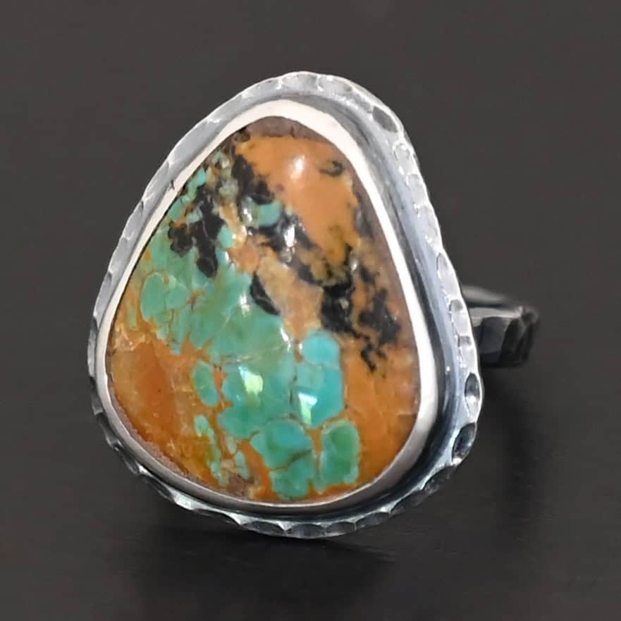 Denver Ring "Denver" Ring. There is a mostly oval turquoise in the center with hammered sterling silver around it. Ring is against a black background.