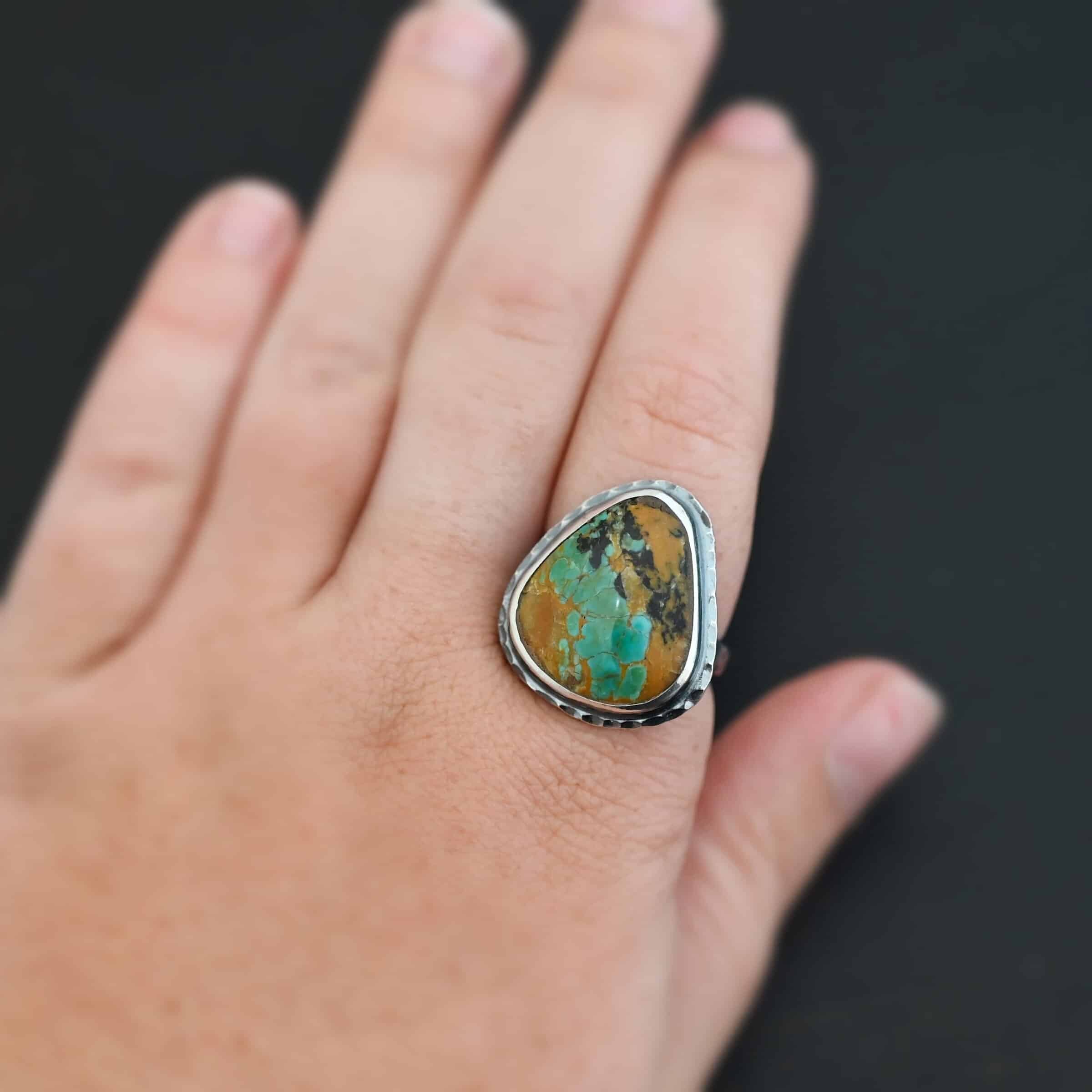 Denver Ring "Denver" Ring. There is a mostly oval turquoise in the center with hammered sterling silver around it. Ring is worn up close by a model.