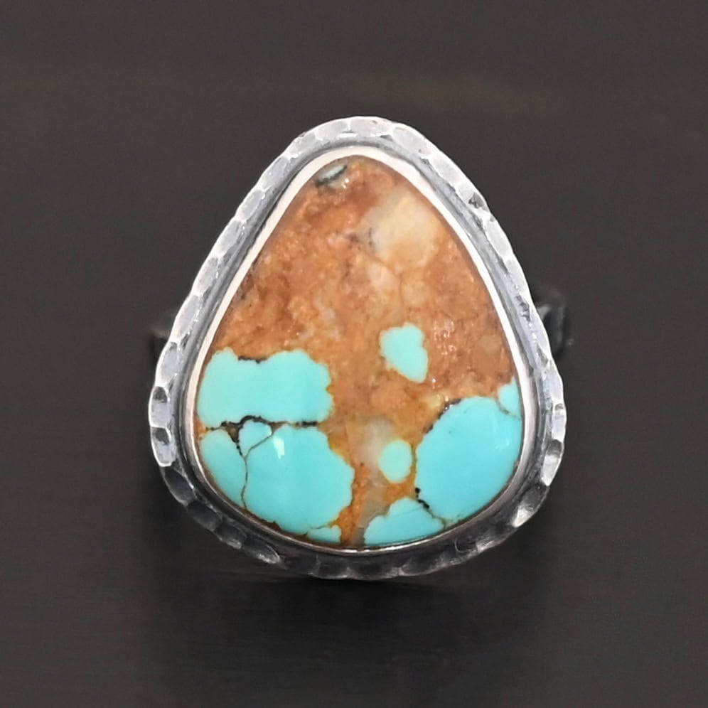 "Arleen" Ring. There is a mostly oval turquoise in the center with hammered sterling silver around it. Ring is set against a black background.