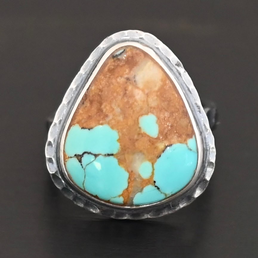 "Arleen" Ring. There is a mostly oval turquoise in the center with hammered sterling silver around it. Ring is set against a black background.