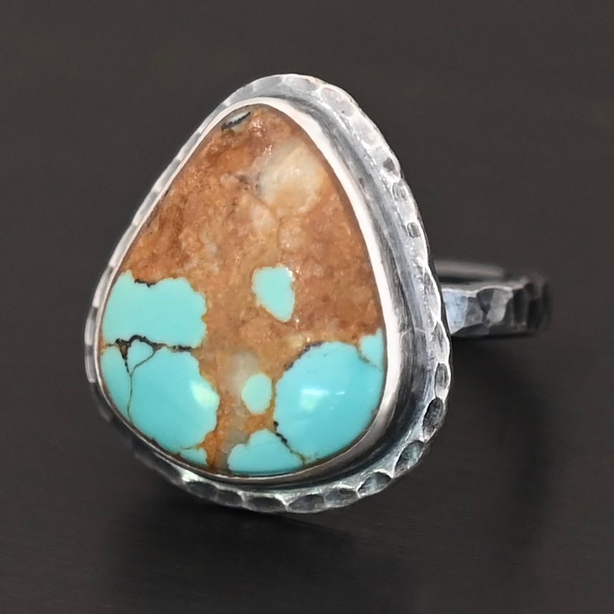 "Arleen" Ring. There is a mostly oval turquoise in the center with hammered sterling silver around it. Ring is set against a black background.