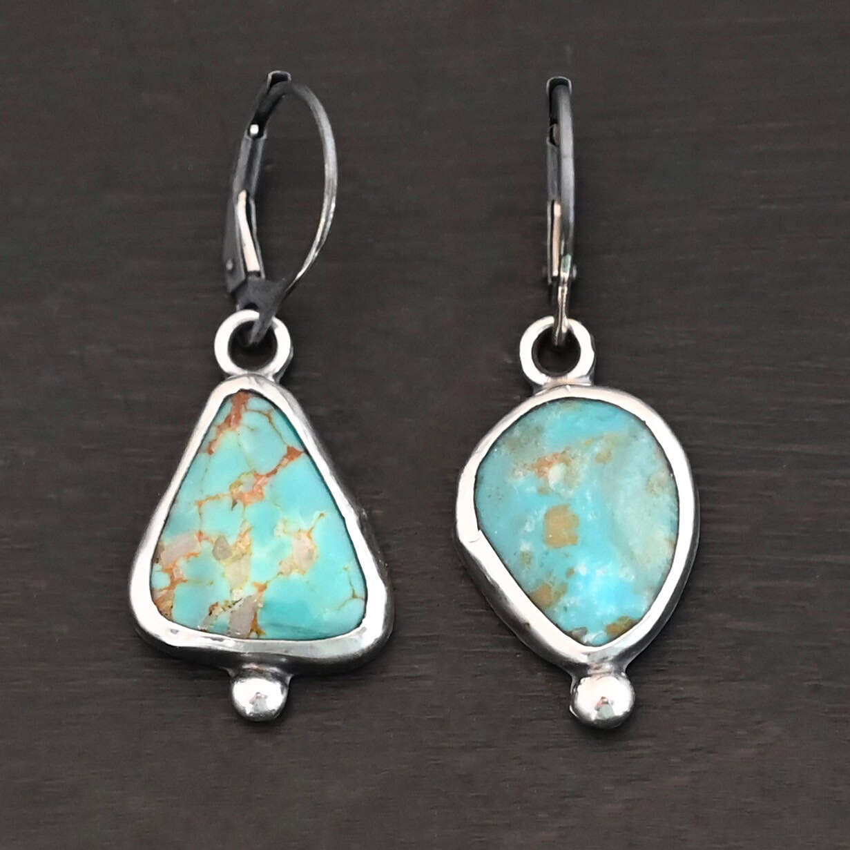 "Ida" Earrings. Sterling Silver & Turquoise. Left earring has a triangular turquoise and right earring has an oval turquoise. Each one has a ball of silver beneath it and silver ear wires.