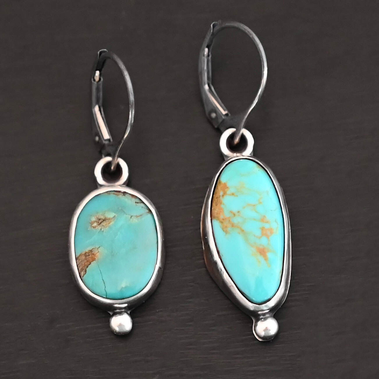 "Vivi" Earrings. Sterling Silver & Turquoise. Left earring has a circular turquoise and right earring is an oval. Each one has a ball of silver beneath it and silver ear wires.