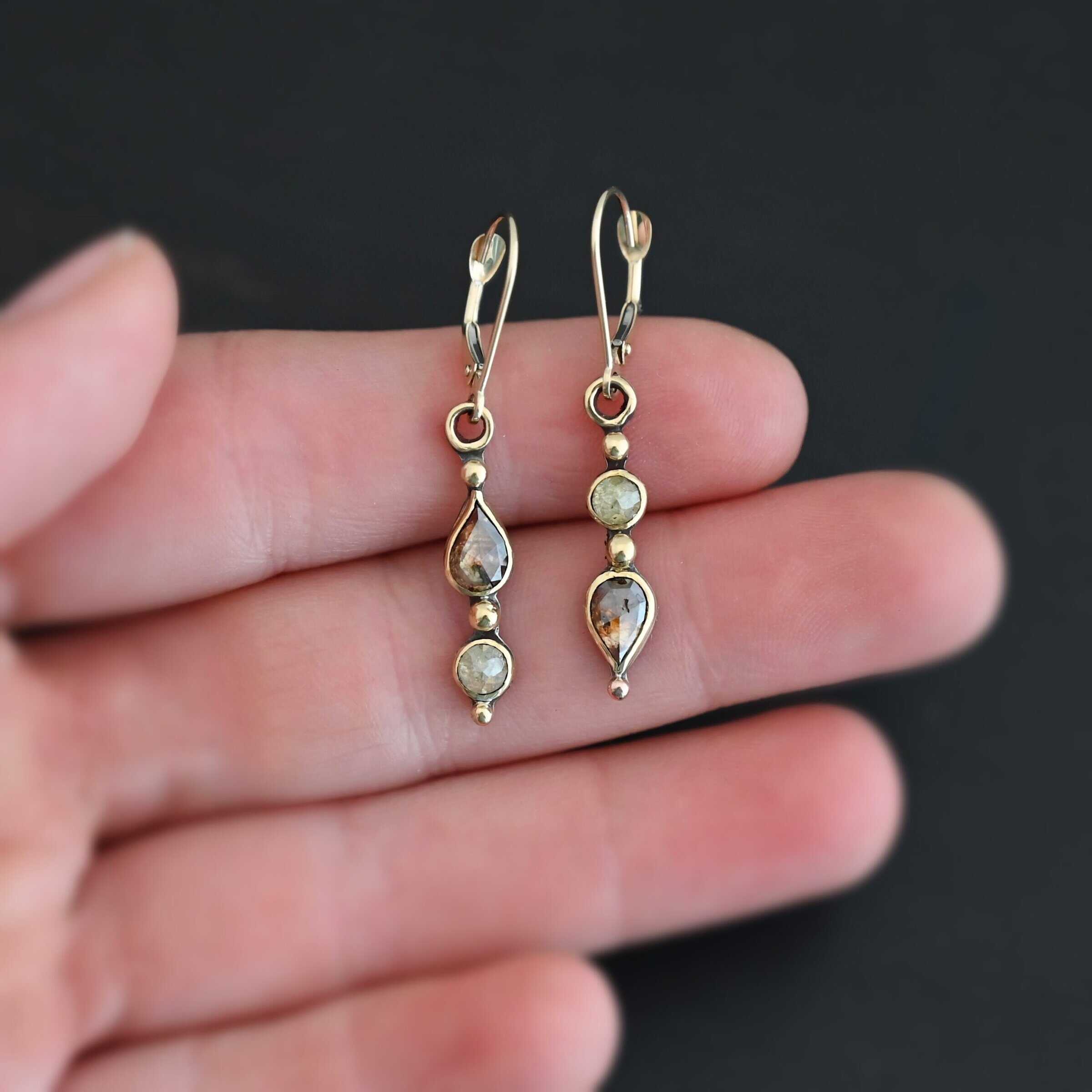 "Solana" Earrings. Gold and Diamonds. Each earring has two brown diamonds. Two teardrops and two circles. The left earring has the teardrop on top and pointing upwards, with the circle beneath it. The right earring has the circle on top and the teardrop beneath, pointing downwards. Each earring has three balls of gold separating the diamonds and above and below them.