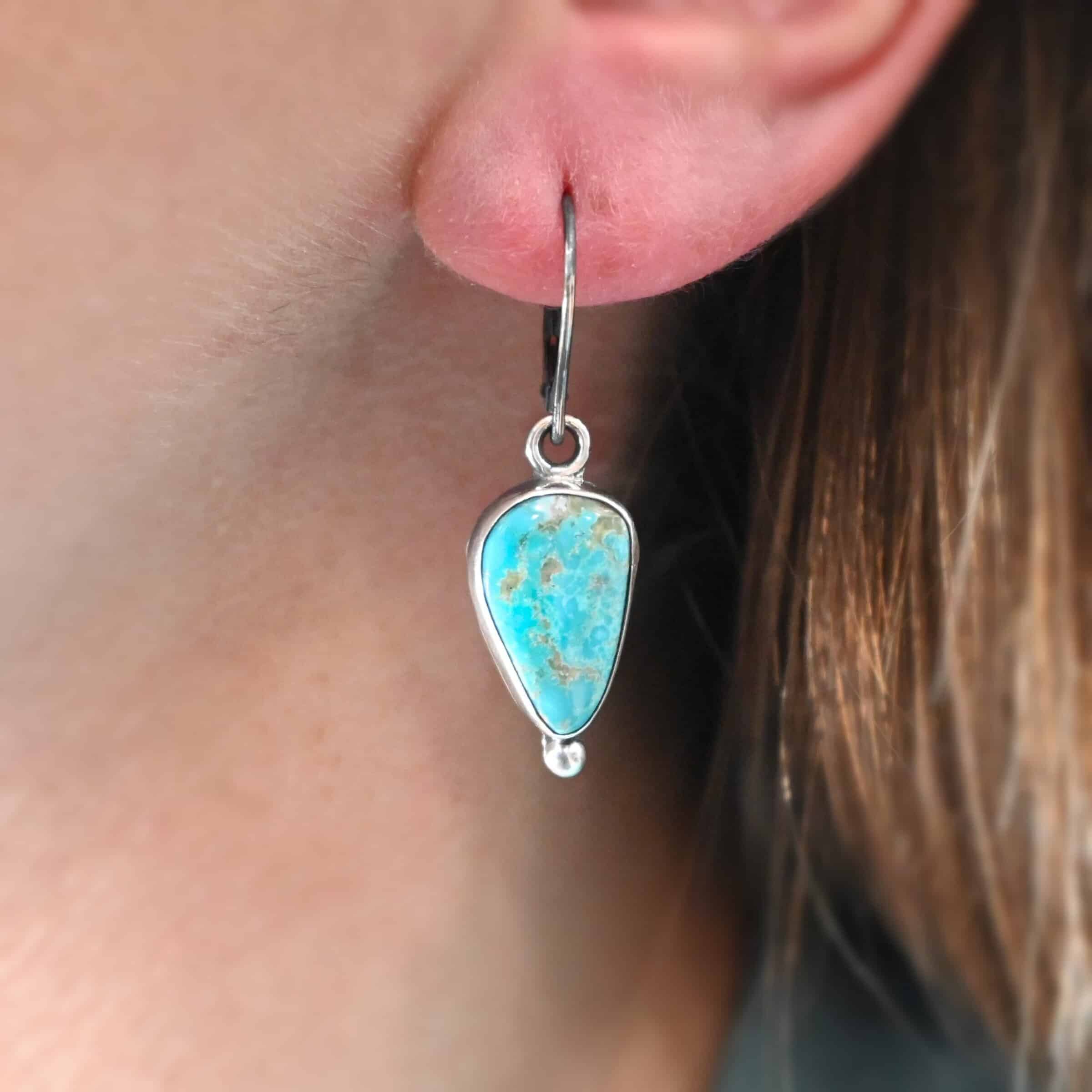 Lottie Earrings "Elma" Earrings. Sterling Silver & Turquoise. Left earring has a triangular shape and right earring is an oval turquoise. Each one has a ball of silver beneath it and silver ear wires.