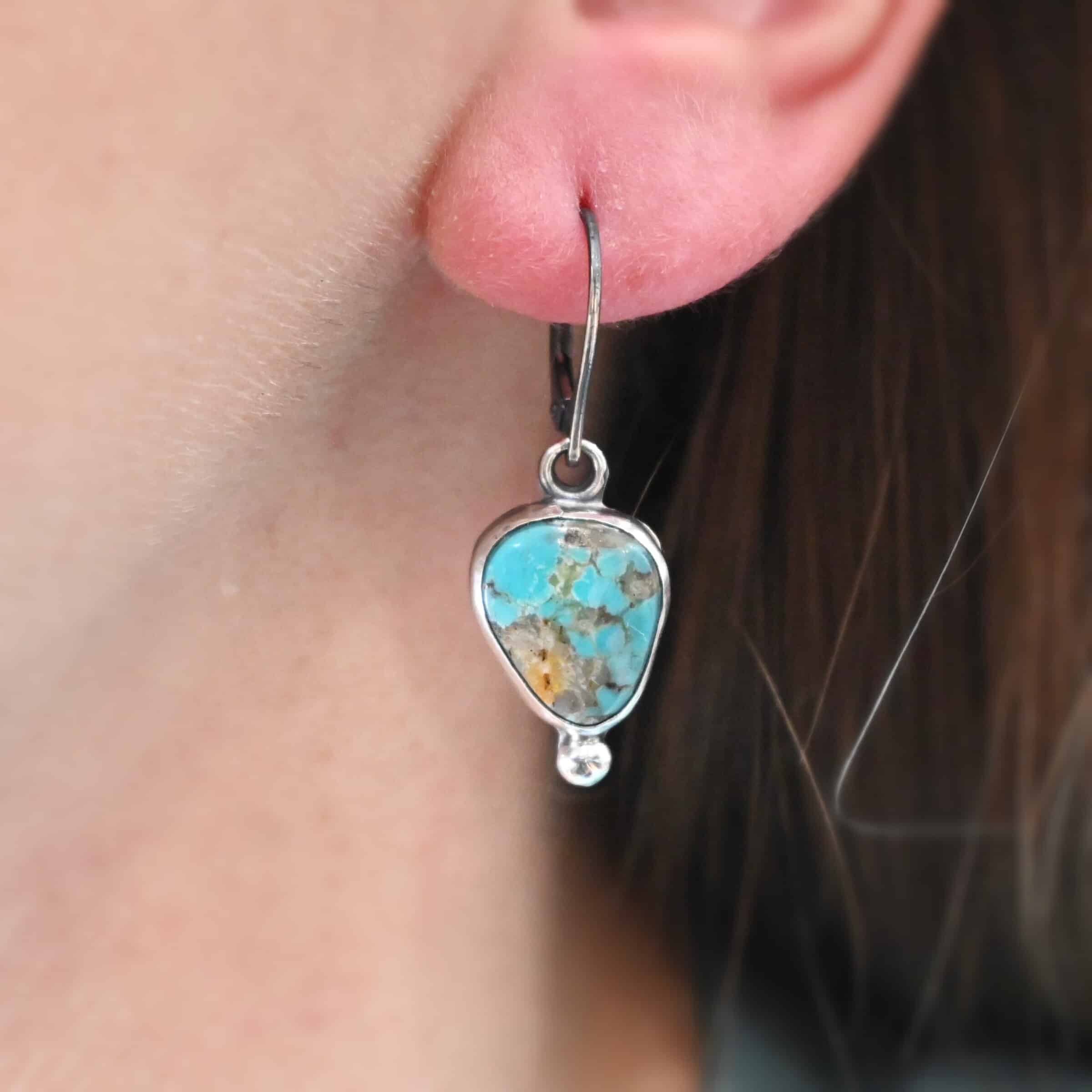 Elma Earrings "Lottie" Earrings. Sterling Silver & Turquoise. Each earring has a primarily oval shaped stone. Each one has a ball of silver beneath it and silver ear wires.