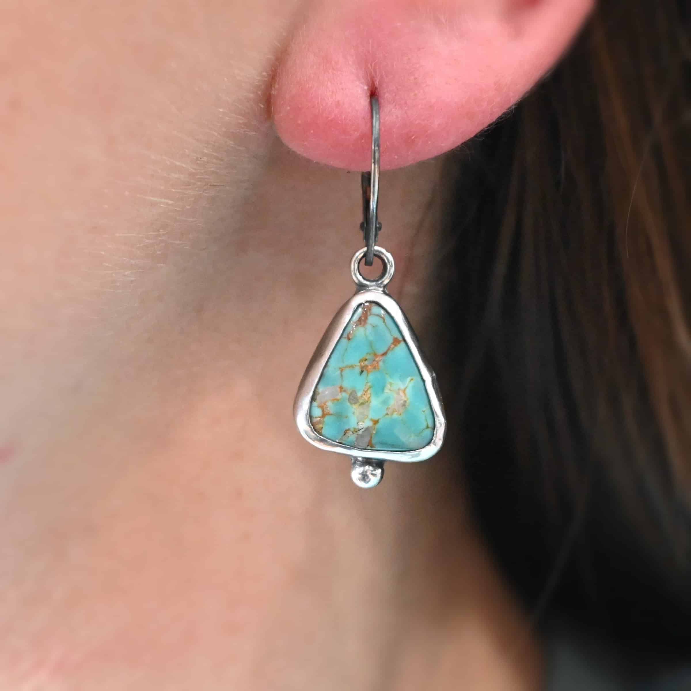 "Ida" Earrings. Sterling Silver & Turquoise. Left earring has a triangular turquoise and right earring has an oval turquoise. Each one has a ball of silver beneath it and silver ear wires.