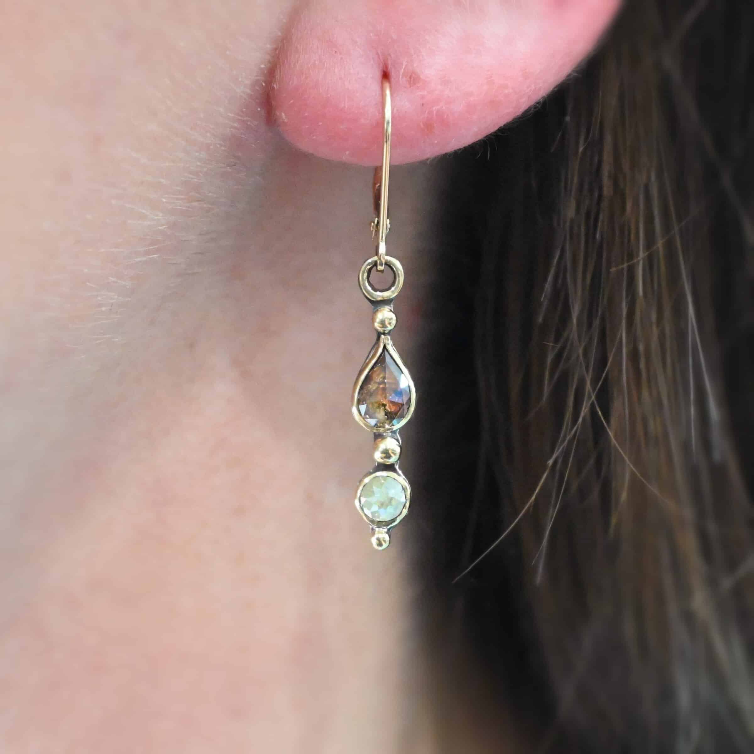 "Solana" Earrings. Gold and Diamonds. Each earring has two brown diamonds. Two teardrops and two circles. The left earring has the teardrop on top and pointing upwards, with the circle beneath it. The right earring has the circle on top and the teardrop beneath, pointing downwards. Each earring has three balls of gold separating the diamonds and above and below them.