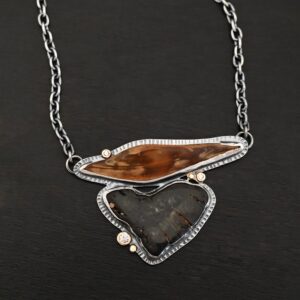 "Sitka" Necklace. There are two mammoth bone fossils. One is horizontal and an oval shape on the top. Soldered beneath it is a primarily triangular one. There are three moissanites scattered around it, set in gold. There are two gold dots on the necklace as well.