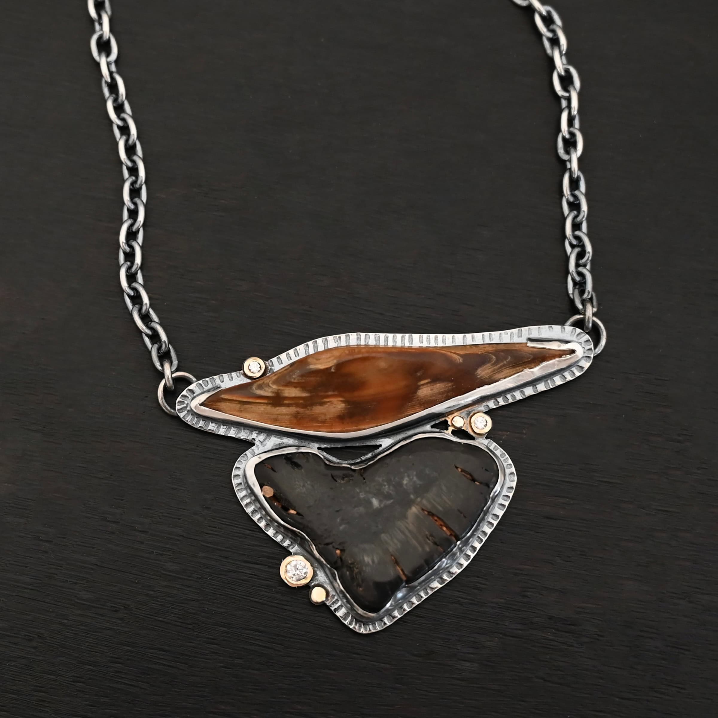 Sitka Necklace "Sitka" Necklace. There are two mammoth bone fossils. One is horizontal and an oval shape on the top. Soldered beneath it is a primarily triangular one. There are three moissanites scattered around it, set in gold. There are two gold dots on the necklace as well.