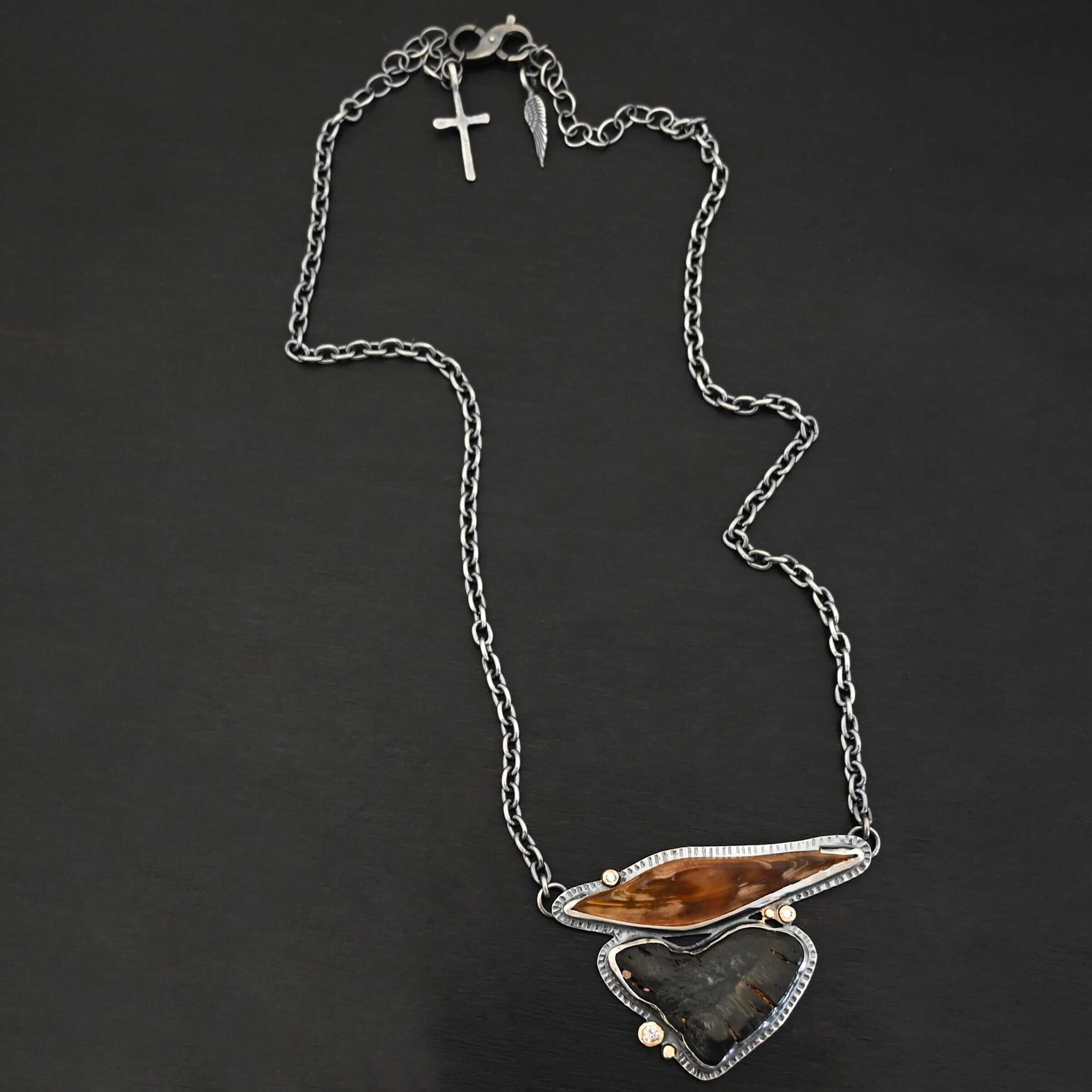 Sitka Necklace "Sitka" Necklace. There are two mammoth bone fossils. One is horizontal and an oval shape on the top. Soldered beneath it is a primarily triangular one. There are three moissanites scattered around it, set in gold. There are two gold dots on the necklace as well.