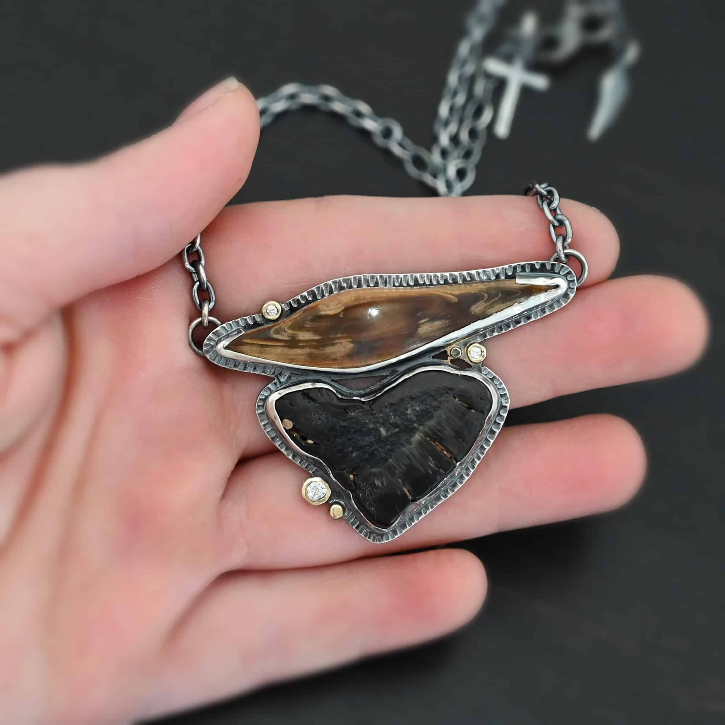 Sitka Necklace "Sitka" Necklace. There are two mammoth bone fossils. One is horizontal and an oval shape on the top. Soldered beneath it is a primarily triangular one. There are three moissanites scattered around it, set in gold. There are two gold dots on the necklace as well.